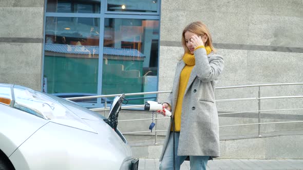 Woman Plugging Her Electric Car To Charge Near Business Center