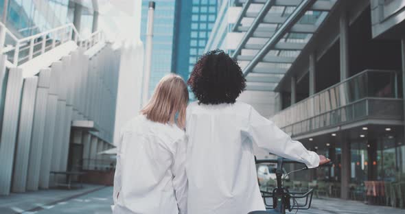 Woman leans on another woman's shoulder and together they look at the view of buildings