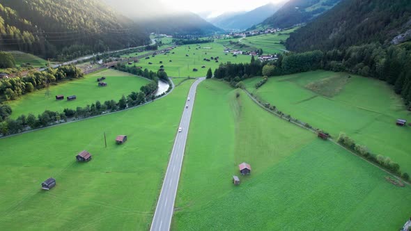 Road in Austrian Alp Valley Between Green Fields and Wooden Houses Aerial View