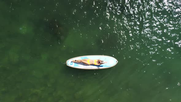 Top View on Blonde Woman in Yellow Bikini Relaxing on the Sup Board