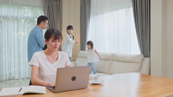 Asian businesswoman working at home due COVID-19 lockdown with young children play around.