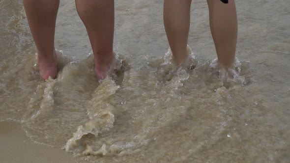 Bare feet of tourists passing along the sandy beach.