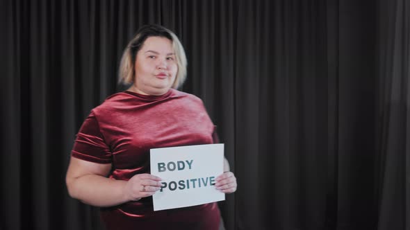 A Confident Flirty Fat Woman Holding a Nameplate with a Sign BODY POSITIVE