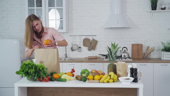 Pretty woman taking out fresh fruit from paper shopping bag at home