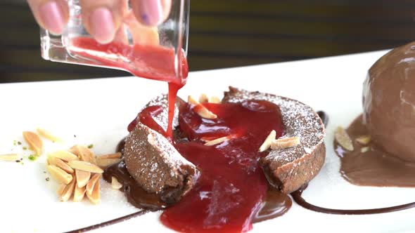 slow motion of hand pouring strawberry sauce into chocolate lava cake