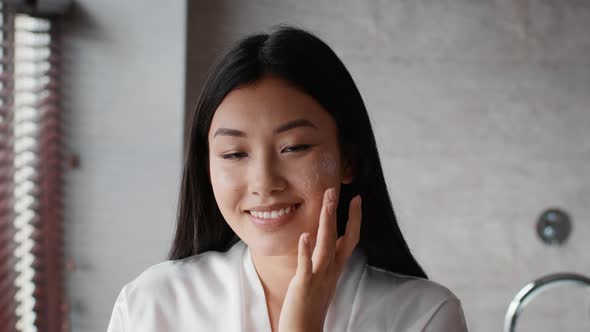 Happy Korean Woman Applying Facial Cream Moisturizing Skin In Bathroom