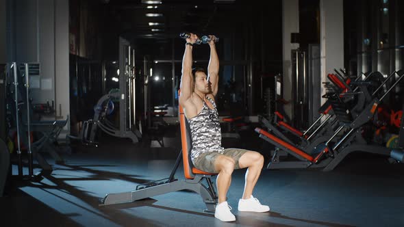 Athletic Muscular Man Working on His Abs Biceps Triceps and Chest With Dumbbells on a Bench in Gym