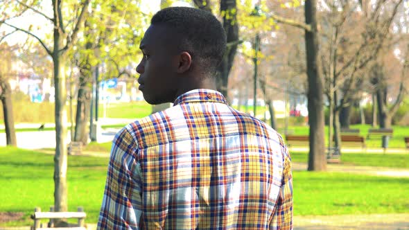 A Young Black Man Waits for Someone with His Back To the Camera in a Park on a Sunny Day