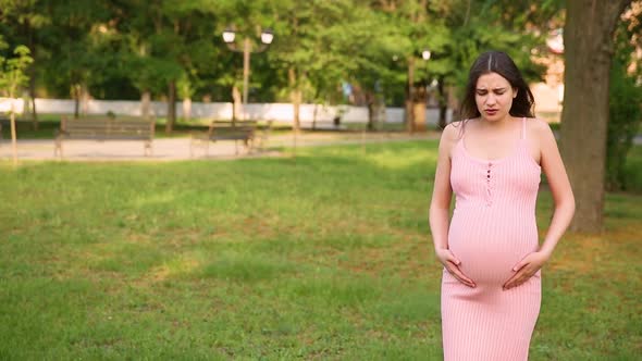 A Pregnant Girl is Standing in the Park and Her Stomach Begins to Hurt