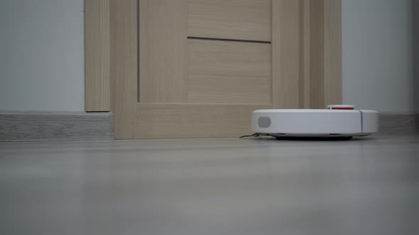 A White Robot Vacuum Cleaner Rides on a White Parquet Floor