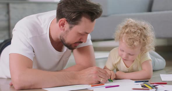 Close Up of a Little Girl and Her Father Who are Drawing on the Floor Father Explains to Daughter