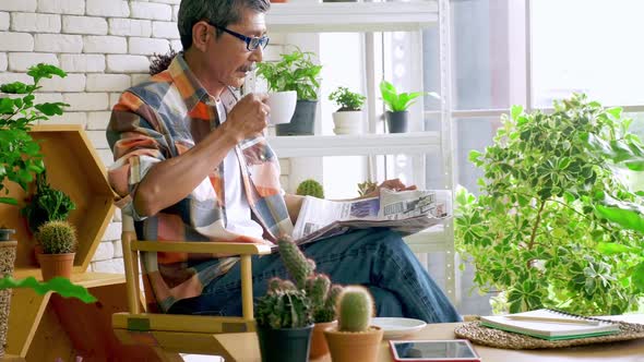 An old man sitting in a living room decorated with flower pots.