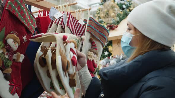 Woman in Medical Mask Chooses Christmas Socks for Gifts in the Mall at the Fair