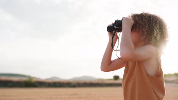 Pretty boy with dreadlocks looking through binocular field glasses and watching nature during sunset