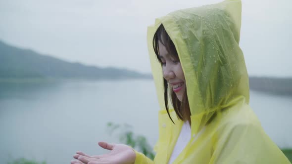 Young Asian woman feeling happy playing rain while wearing raincoat standing near lake.