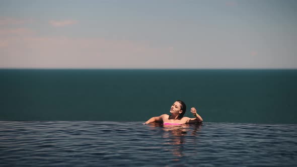 Happy Woman in Swimsuit Swimming in Infinity Pool Against Seafront