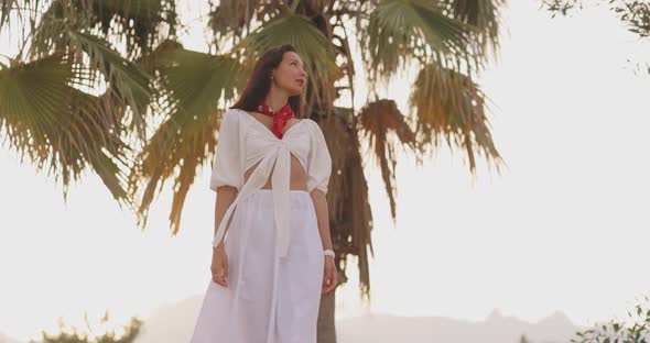 Woman in Elegant Beach Outfit Outdoors Against Palm Trees on the Background During Summer Vacations