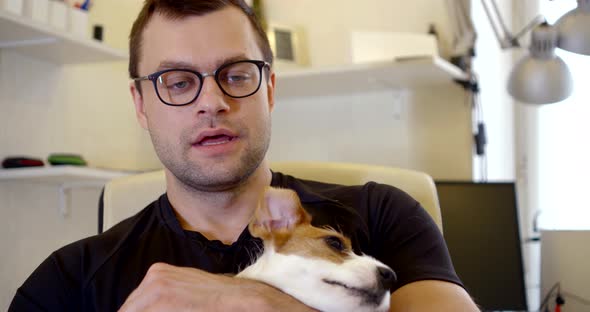 Man Is Giving Interview By Internet, Communicating Through Camera From Home, Stroking His Dog