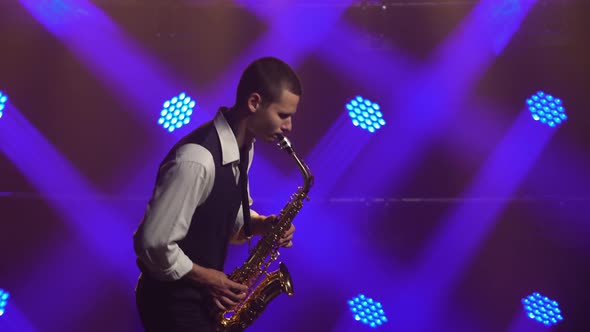 A Young Retro Stylish Guy Plays on the Golden Shiny Saxophone in the Blue Spotlights on Stage