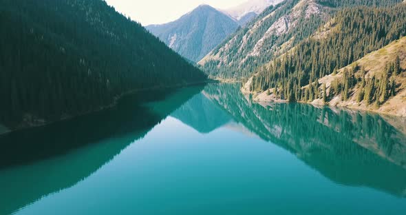 The emerald water of the mountain lake displays coniferous forest, autumn grass, passing clouds.