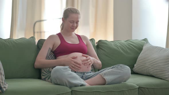 Happy Pregnant Woman Rubbing Her Big Belly While Sitting on Sofa