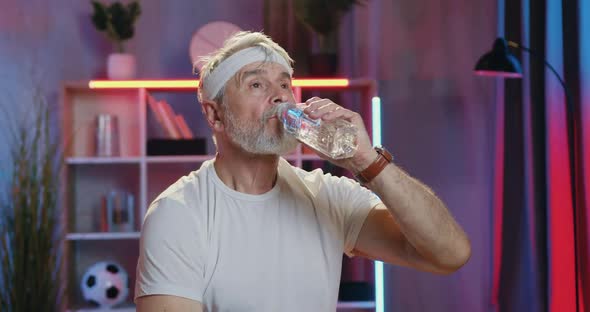 Old Bearded Man in white T-Shirt and White Headband which Refreshing with Water from Bottle