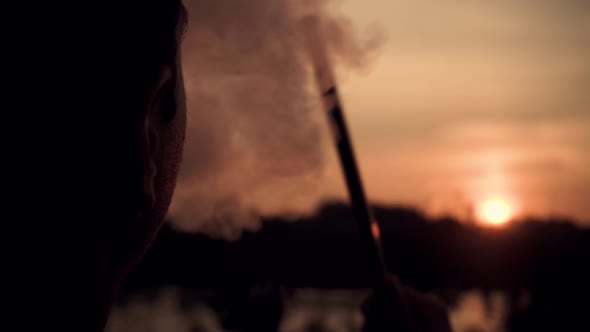 young guy smokes a hookah on a sunset background