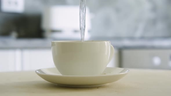 Hot Water is Poured Into a White Cup with Black Coffee in the Kitchen