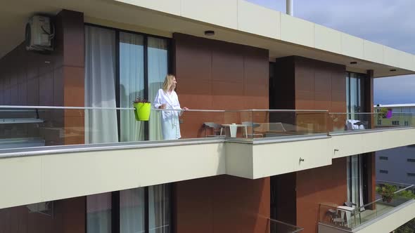 Drone view of woman in white coat with cup of coffee, on hotel balcony