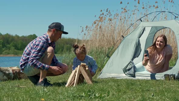 Family is Resting on the Bank of the River with a Tent