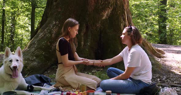 two girls do hand massage in nature under a tree, swiss shepherd dog
