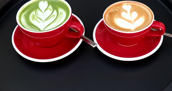 Green tea matcha latte with latte art and cappuccino in red cup on black table.