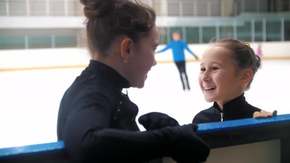 Two Little Girls Figure Skaters Standing By the Side of the Rink and Talking to Each Other