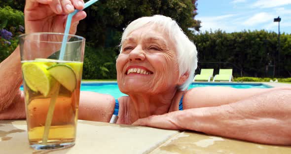 Senior woman having glass of iced tea in pool