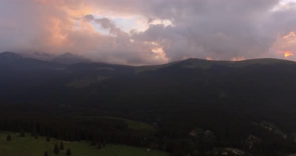 Aerial view of dark moody sunset in the mountains. Green woods and pink skies