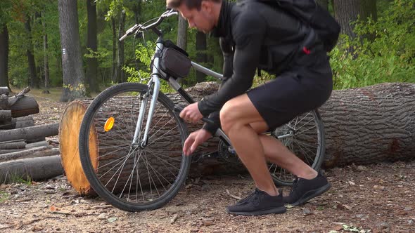 A Young Handsome Cyclist Uses a Pump To Inflate the Front Wheel of His Bike in a Forest