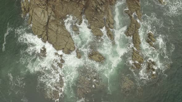 Aerial zoom out of waves swelling and surging against the coastline