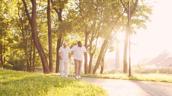 African-American caregiver is teaching disabled old man to walk with walker. Nurse and patient.