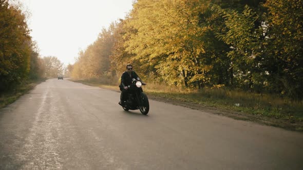 Stylish Young Man in Sunglasses and Leather Jacket Riding Motorcycle on a Asphalt Road on a Sunny