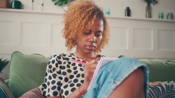 Young African American Woman Artist Draws Sketches in Notebook Sits on Sofa alt