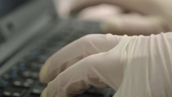 Hand wearing hygienic gloves typing on laptop keyboard close up