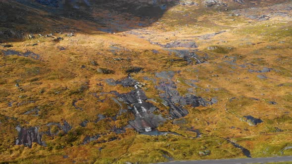 Drone flying back from waterfall in norway. Next to a street and in the mountains.