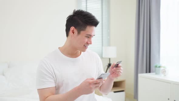 Asian attractive male enjoy shopping online on bed at home in morning.