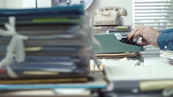 Employee typing with a typewriter and piles of paperwork