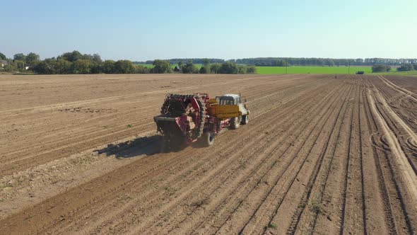 Harvesting Ripe Potatoes With Tractor Trailer Driving Through Rural Field Aerial