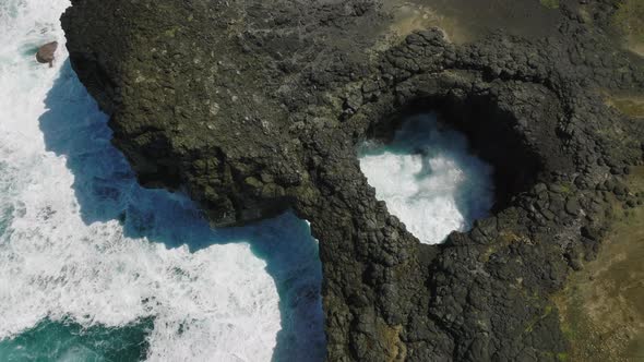 Aerial Top View of Waves Break on Rocks in a Blue Ocean