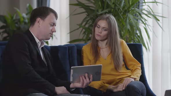 Confident Caucasian Man in Suit Showing Business Presentation on Tablet and Shaking Hand of Female