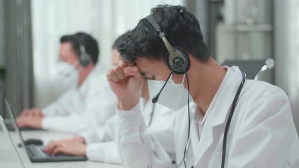 Asian Man Doctor In Masks Working As Call Centre Agent Headache While His Colleagues Working