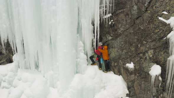 Ice climbers prepare to climb cascade breaking icicles 4K