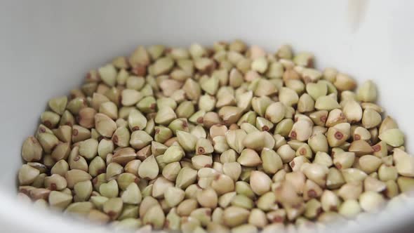 ?lose up uncooked grains of green buckwheat filling a white bowl